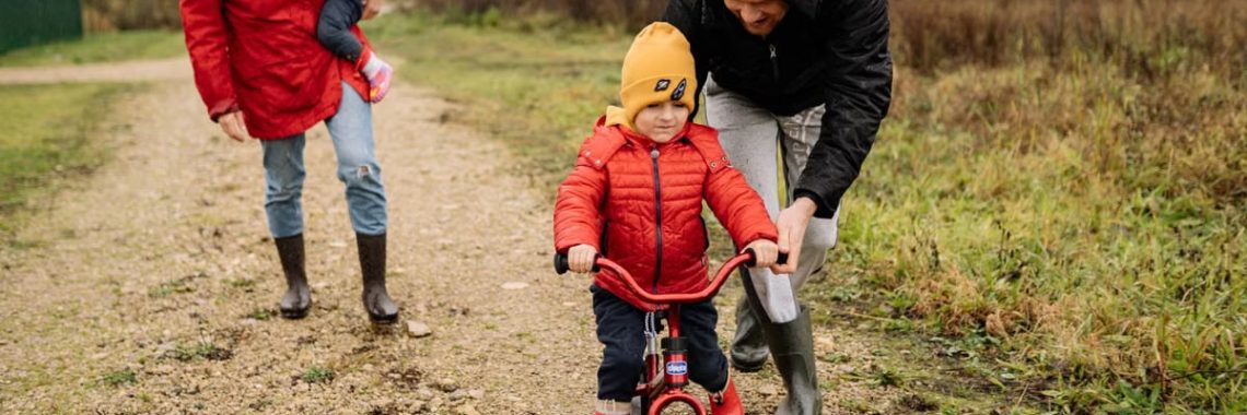 Happy family walking outdoors in fall, teaching child to ride bike.